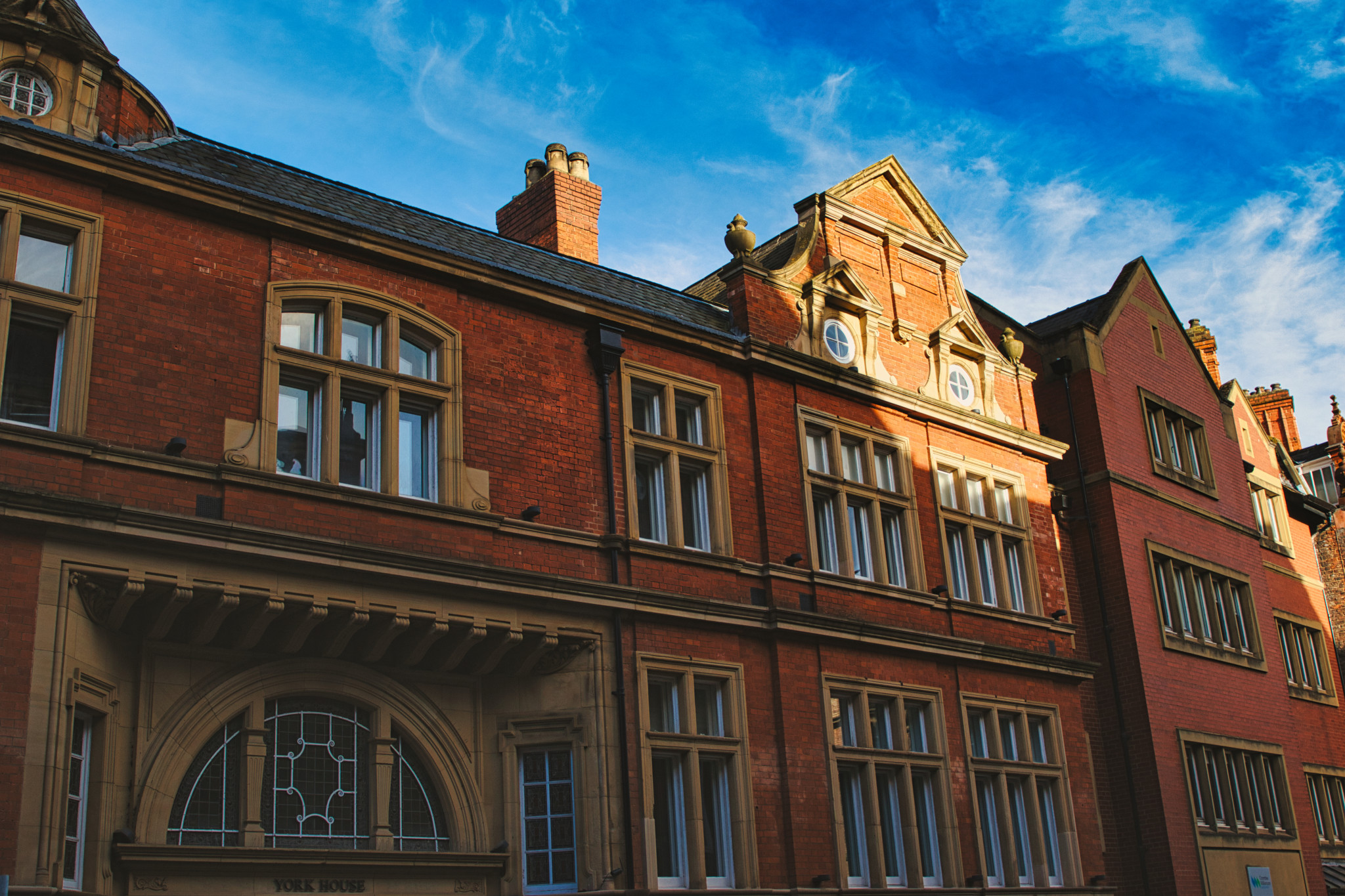 Traditional red brick building with ornate windows under a clear blue sky, showcasing classic architectural details and warm sunlight casting shadows in York, North Yorkshire, England.